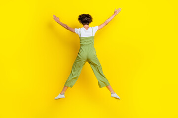 Fototapeta na wymiar Full body size photo of funny woman dressed khaki overalls hands up star positive mood jumping high carefree isolated on yellow color background