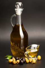 Jug with olive oil, green and black olives on black background.