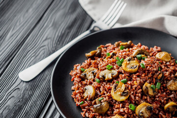 delicious red rice with mushrooms on a black wooden rustic background