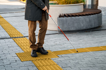 Blind man with a walking stick. Walks on tactile tiles for self-orientation while moving through...