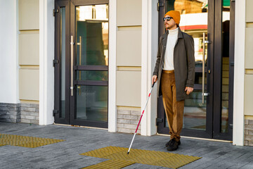 Fototapeta premium Blind man with a walking stick walks out the door into the street