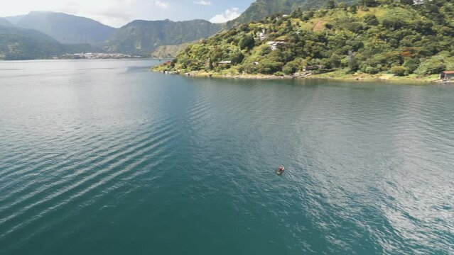 Aerial view of the Atitlan lake with a man sailing in a wooden paddle boat on a sunny day