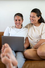 Adult lesbian couple use laptop on couch in living room