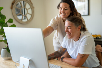 Adult lesbian couple use desktop computer in home office