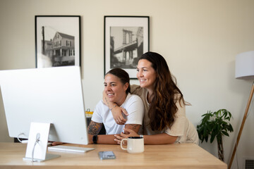 Adult lesbian couple use desktop computer in home office