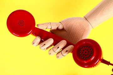 Wooden hand holding a red old fashioned retro telephone handset