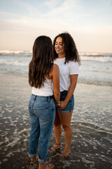 Hispanic lesbian couple hold hands at the beach and stand in the ocean
