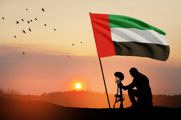 Silhouette of soldier kneeling with his head bowed against the sunrise or sunset and UAE flag....