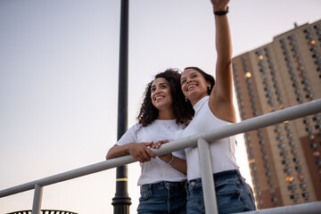 Hispanic lesbian couple lean on the railing at the boardwalk and point