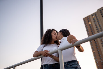 Hispanic lesbian couple lean on the railing at the boardwalk and kiss