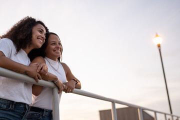 Hispanic lesbian couple lean on the railing at the boardwalk and smile