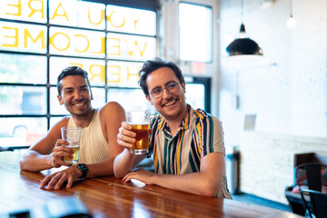 Two LGBTQ friends drink beer at a bar