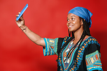 Beautiful black girl with a scarf and typical dress taking a picture with her phone on a red...