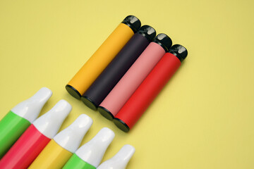 Set of multicolor disposable electronic cigarettes on a bright yellow background.