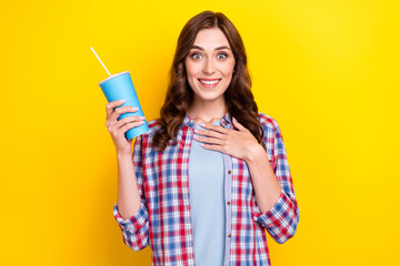 Photo of young funny cute woman wear checkered shirt touch chest unexpected moment film drink soda toothy smile isolated on yellow color background