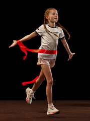 Successfully finishing race. Happy female junior runner in sportswear isolated on dark background....