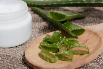 Obraz na płótnie Canvas Aloe Vera leaf cut into pieces on a wooden spoon, next to natural cosmetics. The concept of using natural cosmetic products with natural ingredients.
