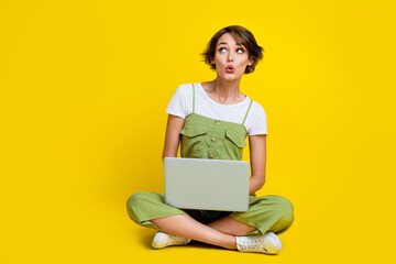 Full size photo of cute young lady work netbook look impressed empty space wear trendy khaki clothes isolated on yellow color background