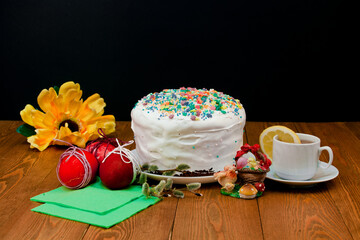 Obraz na płótnie Canvas Homemade Easter cake.White glaze.bread pie, cake. decorated with sweets.a white mug of tea. rose flowers. on a rustic wooden background. with Easter red eggs. spring flowers. happy Easter.meal 