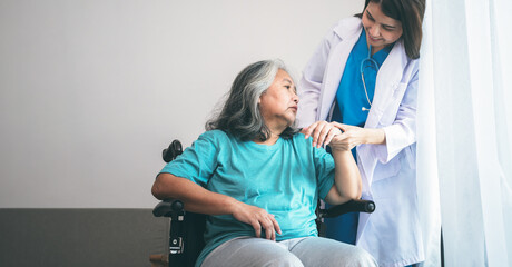 Asian woman doctor take care and encourage elderly patient Which sat on wheelchair, which she is saddened from depression. to elderly and health care concept. - obrazy, fototapety, plakaty