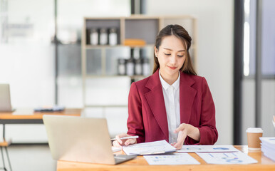 Asian woman working laptop in workplace, Business woman wearing red jacket suit busy working on laptop computer checking finances, investment, economy, saving money or insurance concept