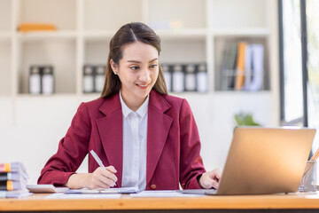 Asian woman working laptop in workplace, Business woman wearing red jacket suit busy working on laptop computer checking finances, investment, economy, saving money or insurance concept