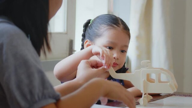 Asian girl is modeling a wooden toy airplane with her parent assistance