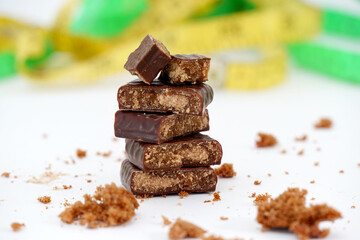 pieces of a filled chocolate in front of a green and yellow blurred measuring tape diet and healthy living concept image