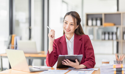 Asian Businesswoman Using laptop computer and working at office with calculator document on desk, doing planning analyzing the financial report, business plan investment, finance analysis concept.