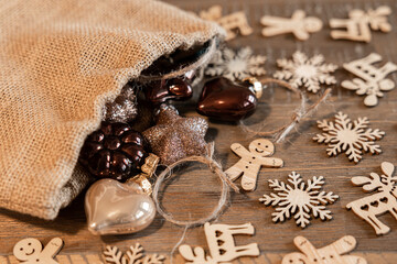 A canvas bag with glass Christmas tree decorations and wooden Christmas decorations lie on an aged wooden table