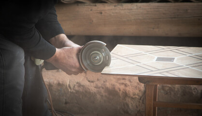 Worker cutting a ceramic tile with a grinder.