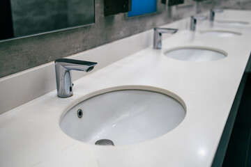 a row of washstands in a public toilet, an automatic water faucet