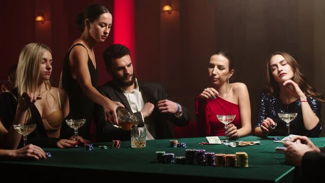 Bearded man and young women stare at their poker playing cards, make bets while playing in the casino. Entertainment industry and luxury lifestyle. The concept of gambling in the casino and poker.
