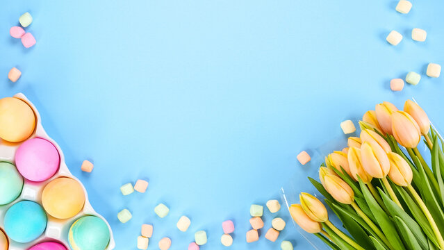 Spring flat lay with fresh yellow tulips colorful eggs on blue background. Easter, Mother day, birthday or Anniversary with copy-space. Sweet rainbow color Easter eggs, small pastel marshmallows.