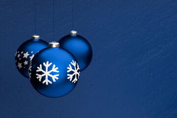 Classic blue christmas baubles with different designs hanging in front of a classic blue stone...