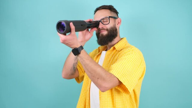 Crazy emotions. Young funny hipster tourist looking through a spyglass and considering the sights isolated on studio background. Looking for discounts, sale, seasonal sales. Colorful summer concept.