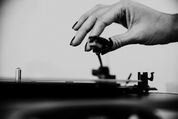 Grayscale closeup shot of a woman  putting the tonearm on a vinyl disk to play music