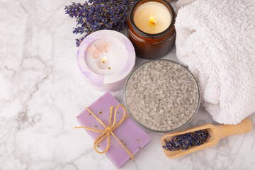 Fototapeta na wymiar Lavender flowers, fragrant sea salt, body cream and candle. The concept of spa, beauty and health salon, skin care cosmetics. Natural cosmetics.Aroma procedures. Closeup on white marble background.