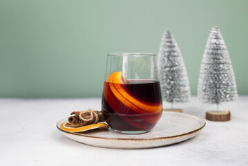 Mulled wine with orange in a glass on a plate on grey and green background.
