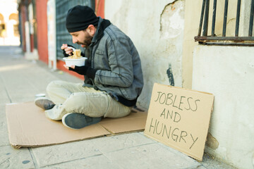 Homeless beggar eating sitting on a cardboard on the street