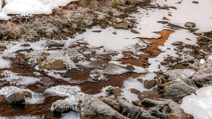 Winter landscape with snow-covered rocks and grass on the river bank