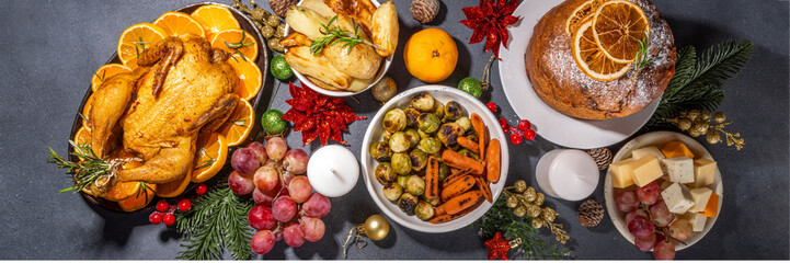 Christmas or New Year dinner foods on dark table. Set of traditional Xmas party dishes - pannetone, baked chicken, vegetables, potato, cheese and fruits plate, top view copy space