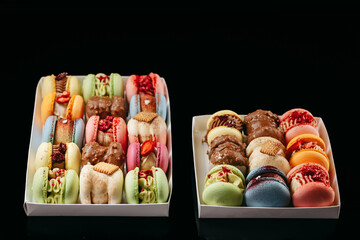 Gift set of large colored macaroons with different fillings and decorations, on a black isolated background. Confectionery concept.