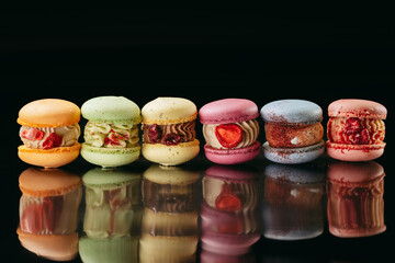 A set of large macaroons of different colors and different fillings. On a black isolated background. Macaroons in a row.