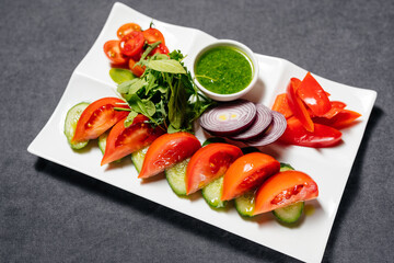 Vegetables, cut into circles, on a plate, sprinkled with greens and green paste. Tomatoes, cucumbers, peppers and arugula.