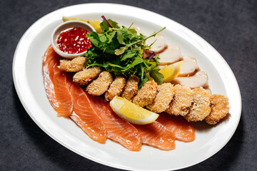 Assorted fish with salmon and fatty fish. On a large white plate. Garnish with a slice of lemon and herbs. View from above. On a gray concrete background.