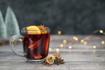 Mulled wine with orange in a glass on dark and brown with lights background. Christmas drink.