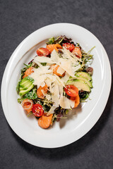 Salad with avocado and salmon on a white plate, decorated with parmesan slices. Restaurant concept.