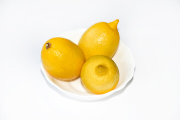Yellow juicy lemons in a white saucer. Delicious yellow lemons on a white background. Beautiful lemons on a plate.