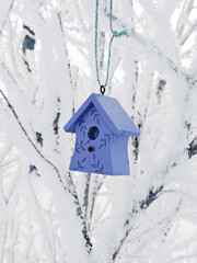 Cute decorative birdhouse hanging on snow-covered branches, closeup
